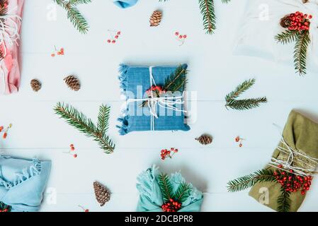 Vista dall'alto concetto di natale zero Waste. Scatole regalo avvolte in tessuto con ramificazione di abete rosso e bacche rosse su fondo di legno bianco con naturale Foto Stock