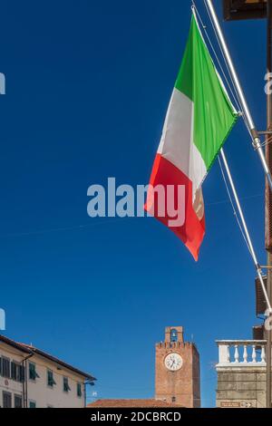 Vista verticale della strada principale del centro storico di Cascina, Pisa, Italia, con la bandiera italiana e la torre dell'orologio in una giornata di sole Foto Stock