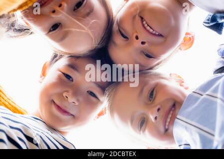 Vista dal basso di bambini multietnici che sorridono alla telecamera isolata bianco Foto Stock