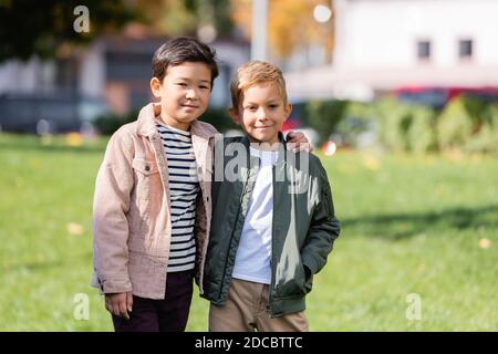 Sorridente ragazzo asiatico abbracciando amico nel parco Foto Stock