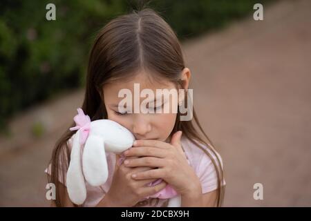 Triste sconvolto caucasico ragazza abbracciare giocattolo. I bambini abbracciano un morbido orso peluche nel parco all'aperto. Ha perso solo il bambino fuori. Infelici problemi di infanzia più vita Foto Stock