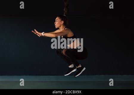 Vista laterale dell'atleta che salta in palestra, riscaldando il corpo Foto Stock