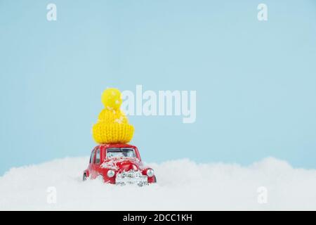 Auto rossa di Natale con cappello giallo lavorato a maglia in un paesaggio innevato. Spazio per il testo. Concetto di carta Happy New Year Foto Stock