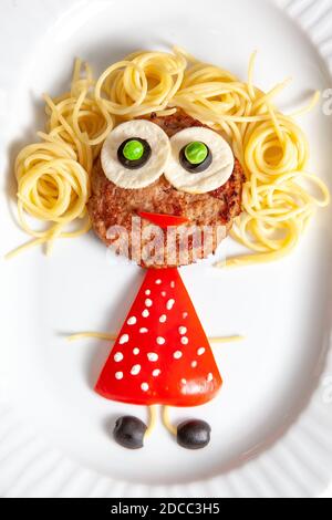 Menu per bambini. Cibo salutare per i bambini. Cotolette, spaghetti, verdure, cucinate vivaci e allegre. Ragazza divertente in un abito rosso con polka bianca Foto Stock