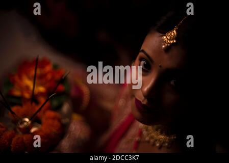 Primo piano ritratto di giovane e bella donna Bengalese indiana in abito tradizionale indiano che celebra Diwali con fiori in fondo scuro. Foto Stock