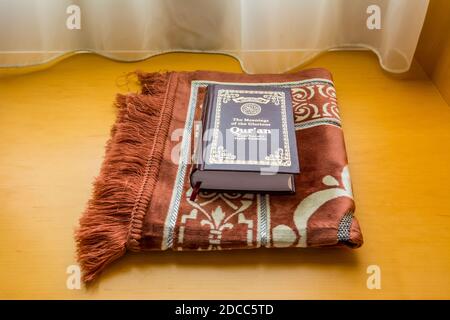 Un libro di agrifoglio del Quran su un tappeto arabo tradizionale a. la finestra sotto la luce del sole nella camera dell'hotel Foto Stock