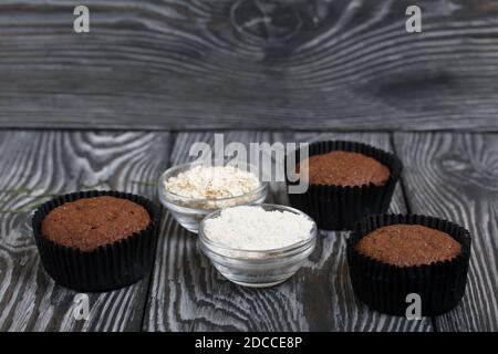 Muffin al cioccolato con farinata d'avena. Disegnato su un piatto d'argento. Uno è rotto per mostrare un taglio. Nelle vicinanze si trovano cereali e farina di avena. Su assi di pino nero. Foto Stock