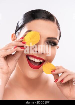 La donna caucasica sorriante toothy tiene le foglie gialle vicino al viso come le macchie. Concetto di bellezza. Isolato su sfondo bianco. Primo piano Foto Stock