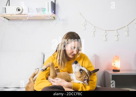 La giovane donna abbracca il suo cane, scena della camera da letto interna. Gioia da animali domestici a casa o durante il blocco o l'isolamento, freddo stagione invernale Foto Stock