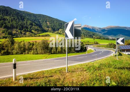 Le indicazioni stradali indicano una curva in un ponte sul fiume Rom nella Val Müstair svizzera. La strada conduce al paese di Müstair e poi al confine italiano. Foto Stock