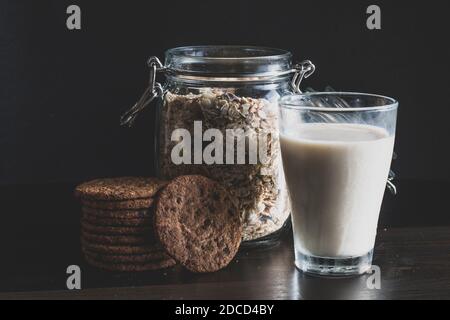 Serve una sana colazione mattutina con muesli a grani interi in fiocchi di mais, latte fresco in un bicchiere e pile di deliziosi biscotti al cioccolato fatti in casa Foto Stock