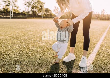 Una madre insegna al suo giovane figlio a camminare, tenendo le mani, all'aria fresca sullo sfondo dell'alba Foto Stock