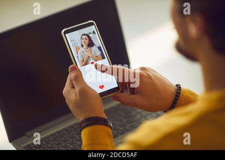 Uomo singolo che guarda la foto della giovane donna graziosa sulla datazione e premendo il pulsante mi piace Foto Stock