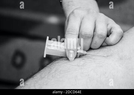 Primo piano monocromatico della siringa che tiene la mano per somministrare la vaccinazione contro il coronavirus. Foto di alta qualità Foto Stock