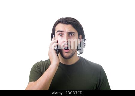 Un giovane scioccato, durante una conversazione con un cellulare, fissando con occhi grandi e la bocca aperta isolato su sfondo bianco. Il ragazzo stupito sente le cattive notizie sp Foto Stock