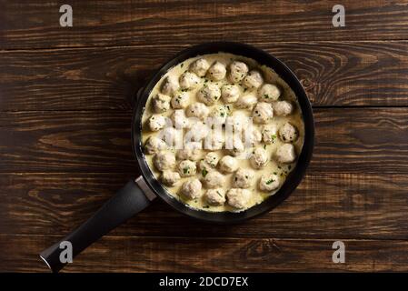 Deliziose polpette svedesi fatte in casa con salsa bianca cremosa in padella su sfondo di legno con spazio libero. Vista dall'alto, disposizione piatta, primo piano Foto Stock