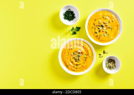 Purea di zucca con semi in ciotola su sfondo giallo con spazio di testo libero. Concetto di alimentazione sana. Vista dall'alto, disposizione piatta Foto Stock