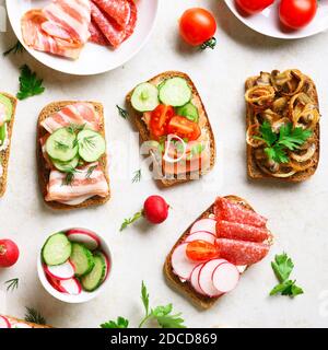 Panini diversi con carne, verdure, frutti di mare su sfondo di pietra chiaro. Snack gustoso. Vista dall'alto, disposizione piatta. Foto Stock