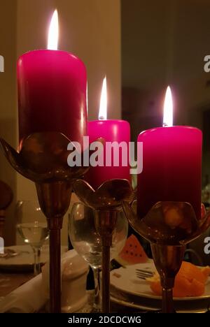 Ancora vita con tre candele rosse in candelabri di rame d'epoca sul tavolo da pranzo nel buio. Fiamme a lume di candela di candele cilindriche di cera rossa. Burnin Foto Stock