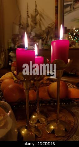 Ancora vita con tre candele rosse in candelabri di rame d'epoca sul tavolo da pranzo nel buio. Fiamme a lume di candela di candele cilindriche di cera rossa. Burnin Foto Stock