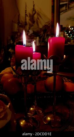 Ancora vita con tre candele rosse in candelabri di rame d'epoca sul tavolo da pranzo nel buio. Fiamme a lume di candela di candele cilindriche di cera rossa. Burnin Foto Stock