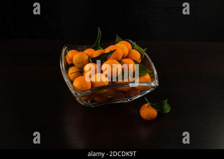 Vaso in vetro con tangerini. Decorazioni per il nuovo anno e il Natale. Si trova in un vaso di vetro su sfondo nero, vista dall'alto. Foto Stock