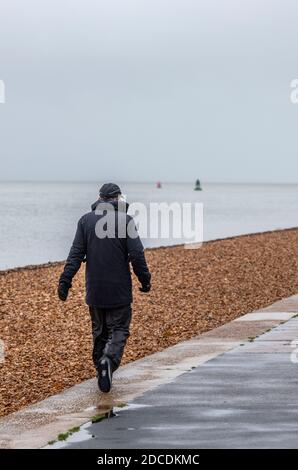 un uomo che cammina da solo sul lungomare sulla costa o sulla spiaggia sotto la pioggia in una giornata bagnata. Foto Stock