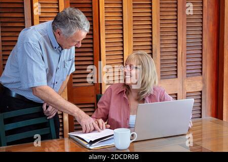 Una donna anziana e un uomo sorridenti e che parlano di carte. La donna è un tavolo con un computer portatile davanti a lei. Foto Stock