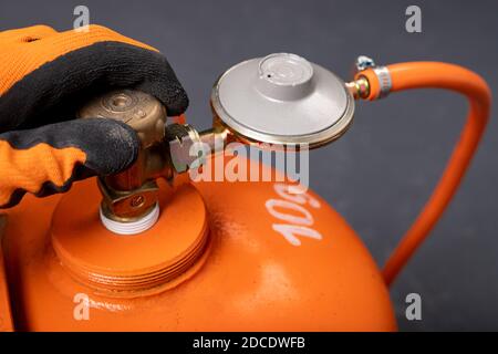 Svitando la bombola di propano-butano. Gas combustibile utilizzato nelle abitazioni. Sfondo scuro. Foto Stock