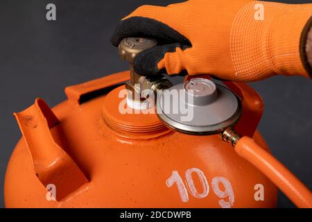 Svitando la bombola di propano-butano. Gas combustibile utilizzato nelle abitazioni. Sfondo scuro. Foto Stock