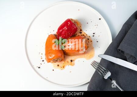 Tre peperoni ripieni di colore arancio e rosso sono stati cosparsi di spezie ed erbe in una piastra piatta bianca. Foto Stock