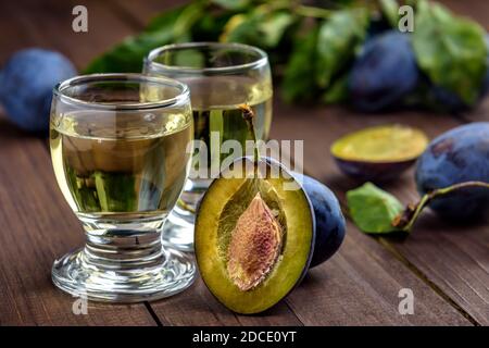 Brandy di prugne o schnapps in bicchieri e prugne fresche gustose su un tavolo di legno. Messa a fuoco selettiva. Foto Stock