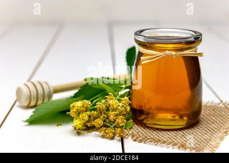 Vaso con miele di tiglio, bastone per miele e fiori di tiglio freschi su un tavolo di legno. Foto Stock