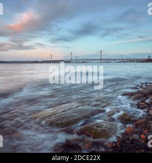 Una costa della baia del mare con pietre al tramonto Vicino al New Queensferry Crossing Bridge in Scozia Foto Stock