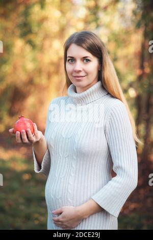 giovane donna incinta che tiene melograno. Foto della crescita fetale 21 settimane di gravidanza. Dieta sana di gravidanza. Concetto di fertilità. Spazio per il testo Foto Stock