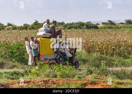 Hosahalli, Karnataka, India - 3 novembre 2013: Triciclo giallo motorizzato sovraccaricato di uomini appesi sul retro e sui lati e seduti sul tetto con estensione Foto Stock