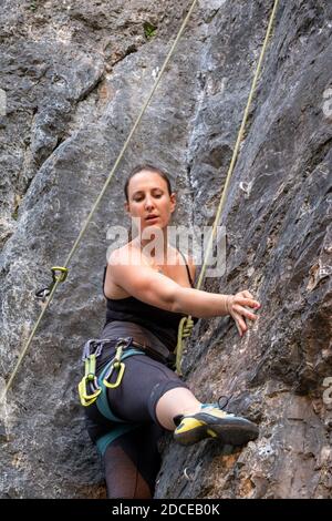 felice bella donna caucasica con lunghi capelli marroni attivamente rock arrampicandosi all'esterno in un paesaggio bello fra gli alberi verdi e. scogliere in una giornata di sole Foto Stock