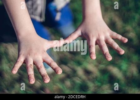 Le mani sporche dei bambini piccoli sul fondo verde dell'erba del parco. Concetto di igiene, primo piano. Foto Stock