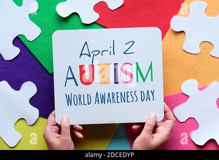 Hands Hold Board. Con testo 2 aprile Autism giornata mondiale di consapevolezza. Puzzle, sfondo in feltro stratificato. Foto Stock