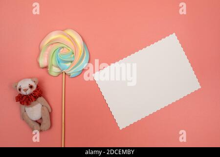 Cartolina bianca vuota, meringa arcobaleno su un bastone e orsacchiotto su sfondo rosa. Natale, Capodanno, San Valentino, Giornata Internazionale della Donna Foto Stock