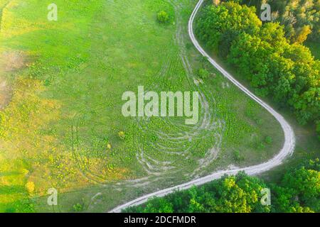 Terra strada sterrata autostrada sul prato vicino agli alberi sul bordo della foresta verde in estate al tramonto con lunghe ombre - scatto aereo con a. posiziona per il testo Foto Stock