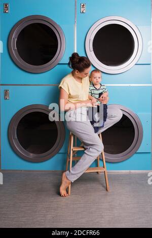 Madre Household con i bambini che hanno divertimento e facendo lavanderia a. Lavanderia self-service vicino alle lavatrici Foto Stock