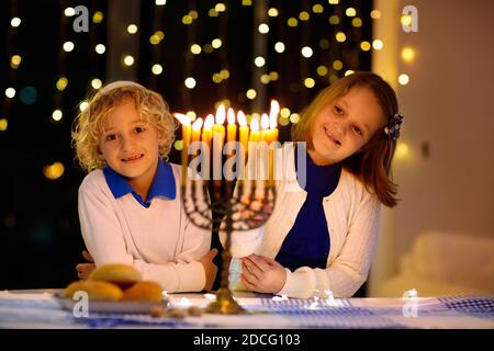 Bambini che celebrano Hanukkah. Festa ebraica delle luci. I bambini illuminano le candele sulla menorah tradizionale. Ragazzo in kippah con dreidel Foto Stock