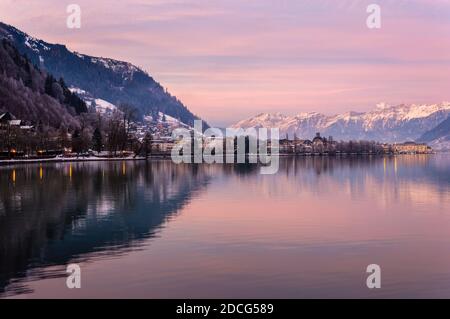 Zell am See in inverno sera. Vista sul lago Zell, città, montagne e neve con riflessi in acqua. Città alpina al crepuscolo viola. Famosa stazione sciistica Foto Stock