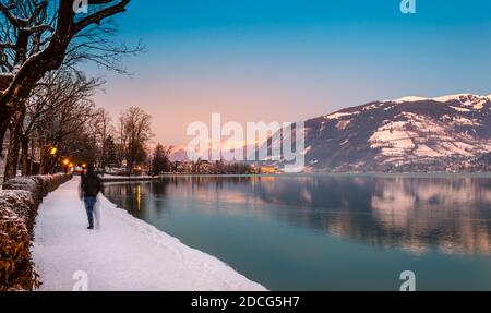 Zell am See in inverno sera. Esplanade lungo il Lago Zell, turistico offuscato, città, montagne e neve con riflessi in acqua. Famosa stazione sciistica Foto Stock