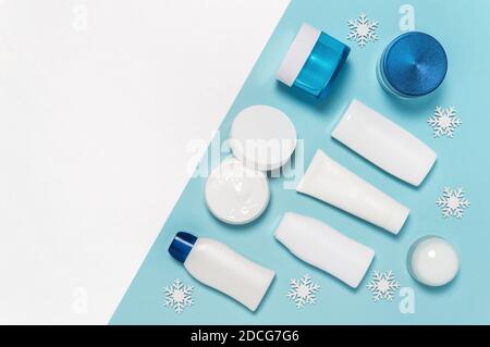 Set di prodotti cosmetici invernali per la cura della pelle su sfondo bianco e blu con fiocchi di neve. Confezione di vasetto, tubetto, lozione per il corpo, latte e biberon detergente Foto Stock