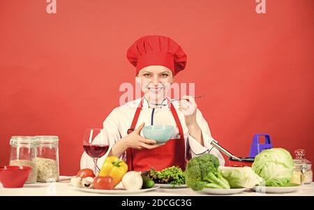 donna in cappello da cuoco. chef professionista su sfondo rosso. donna felice che cucinano cibi sani secondo la ricetta. cibo biologico e vegetariano. Casalinga, menu del ristorante. Dieting. Chi si preoccupa della dieta. Foto Stock