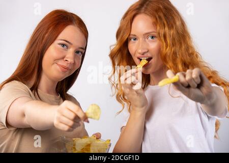 Le ragazze di redhead stanno mangiando le schegge e posando. Foto su sfondo bianco. Foto Stock