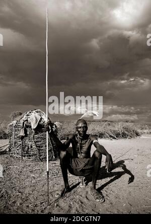 Ritratto di un uomo della tribù dei Pokot seduto sul suo cuscino di legno che tiene una lancia, Baringo County, Baringo, Kenya Foto Stock