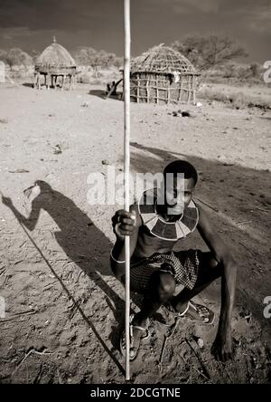 Ritratto di un uomo della tribù dei Pokot seduto sul suo cuscino di legno che tiene una lancia, Baringo County, Baringo, Kenya Foto Stock